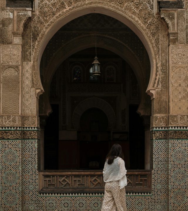 A woman walks by a beautifully decorated archway of a Moroccan mosque in Fes, showcasing traditional Islamic architecture.