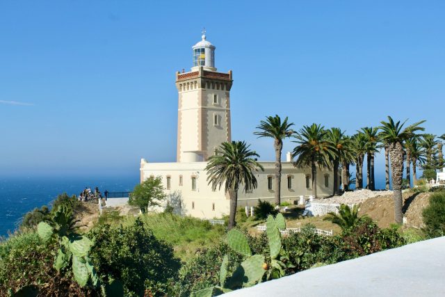 A scenic view of Cape Spartel Lighthouse surrounded by lush palm trees on a sunny day in Morocco.