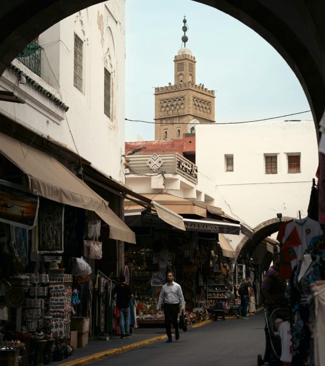 Vibrant street market scene in a historic medina with a mosque tower in the background.