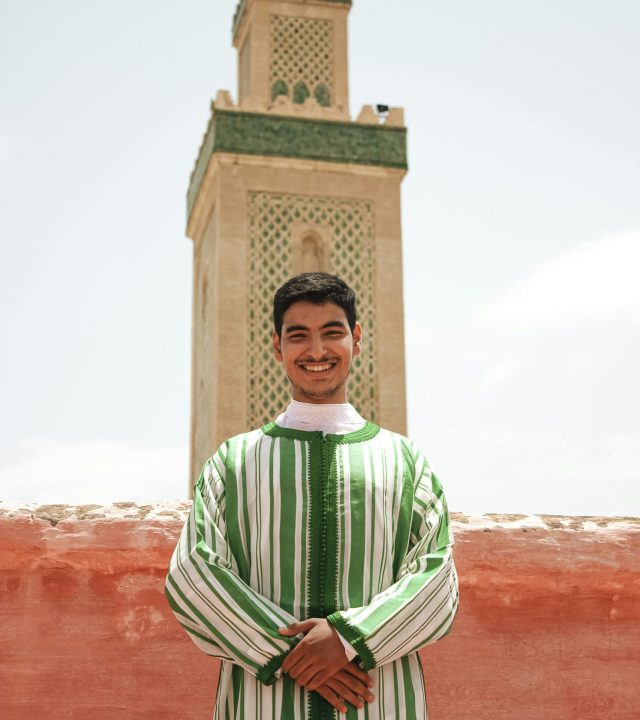 Portrait of a man in Fes wearing traditional Moroccan attire in front of a mosque.