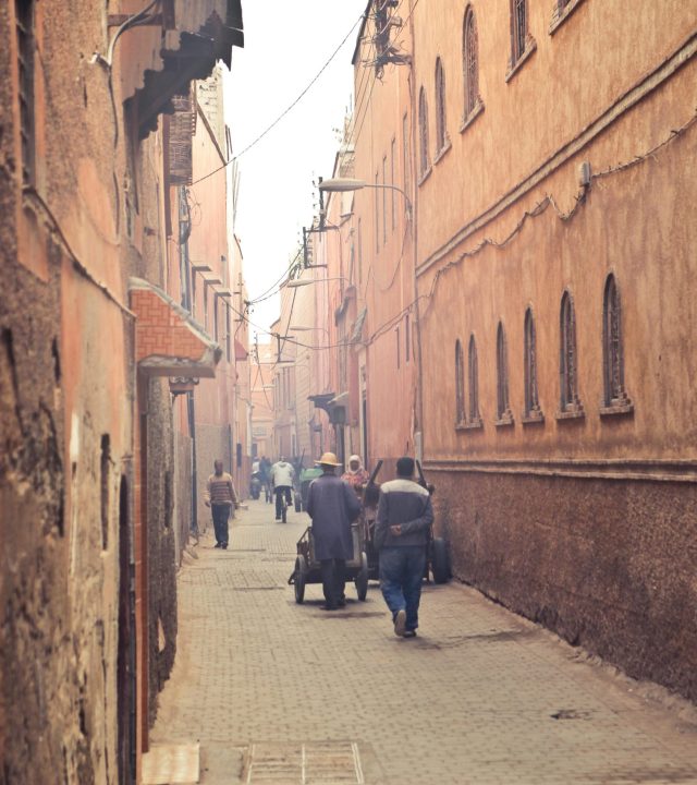 Perspective view of aged narrow street with people walking among ancient oriental buildings in hazy light