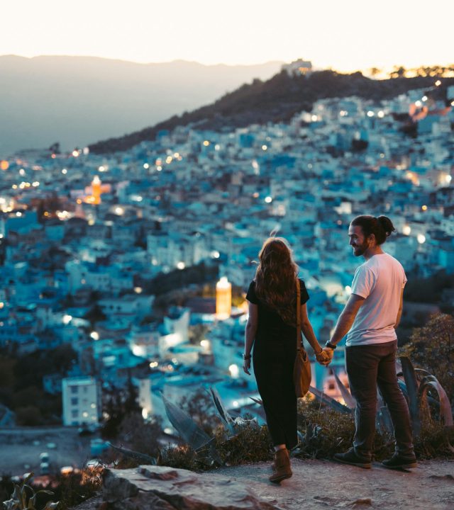 A romantic couple holding hands with a view of Chefchaouen, Morocco at twilight.