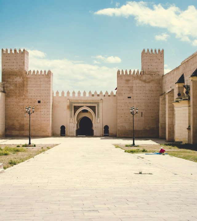 A grand fortress with towering walls and a central archway under a blue sky.